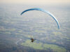 Osoba si užíva adrenalínový let na paraglidingu vysoko nad krajinou.