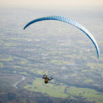 Osoba si užíva adrenalínový let na paraglidingu vysoko nad krajinou.