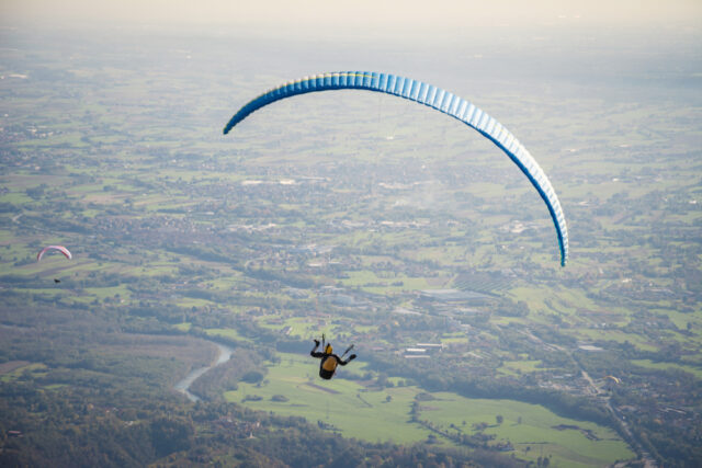 Osoba si užíva adrenalínový let na paraglidingu vysoko nad krajinou.